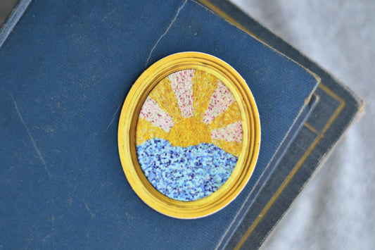 Decorative sticker with a yellow border, pink floral center, and blue speckled bottom on a blue textured surface.